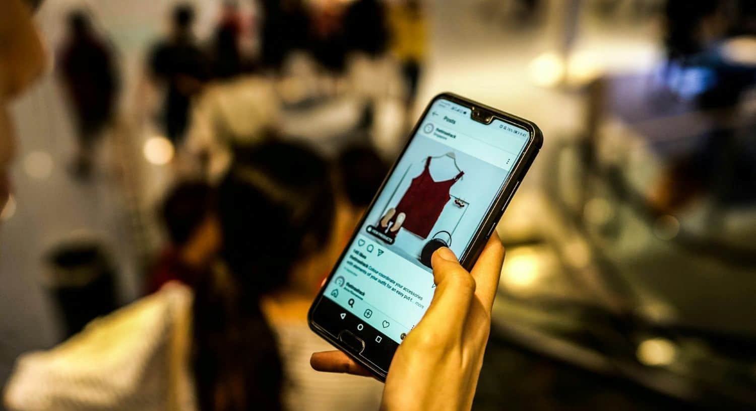 Hand holding a mobile phone with clothing on screen.