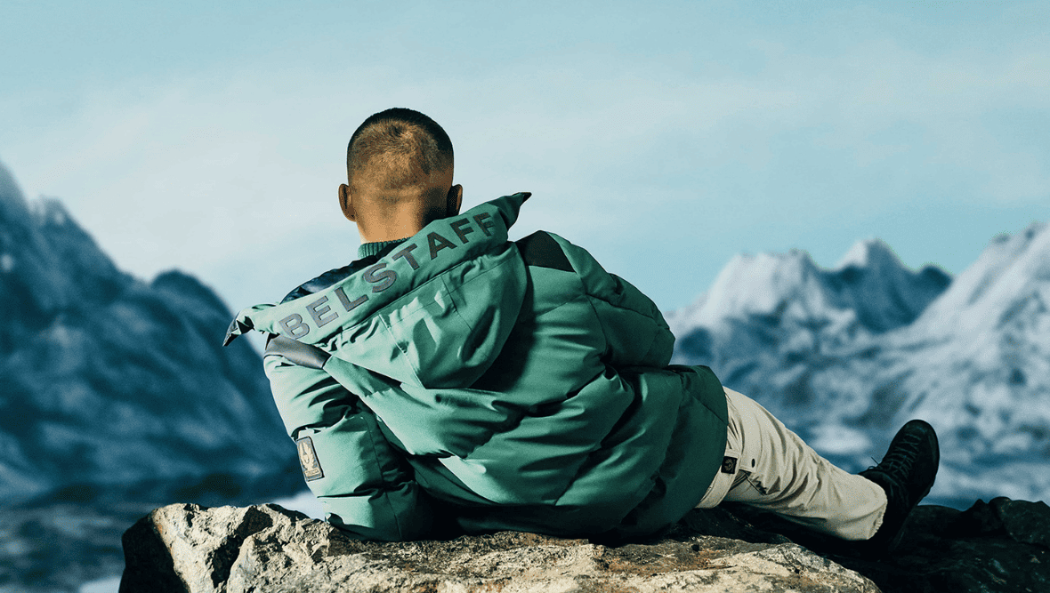 man wearing Belstaff jacket looking out to mountains on horizon