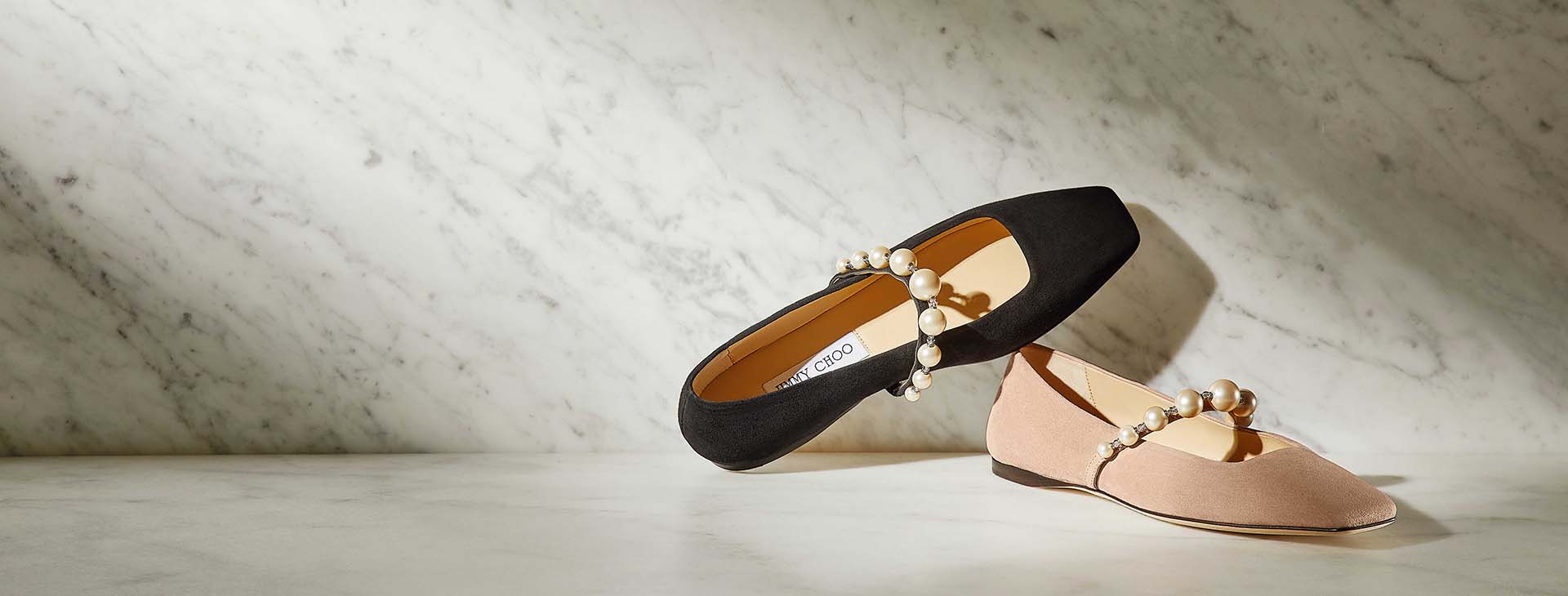 A nude and a black Jimmy Choo ballet pump on marble floor.