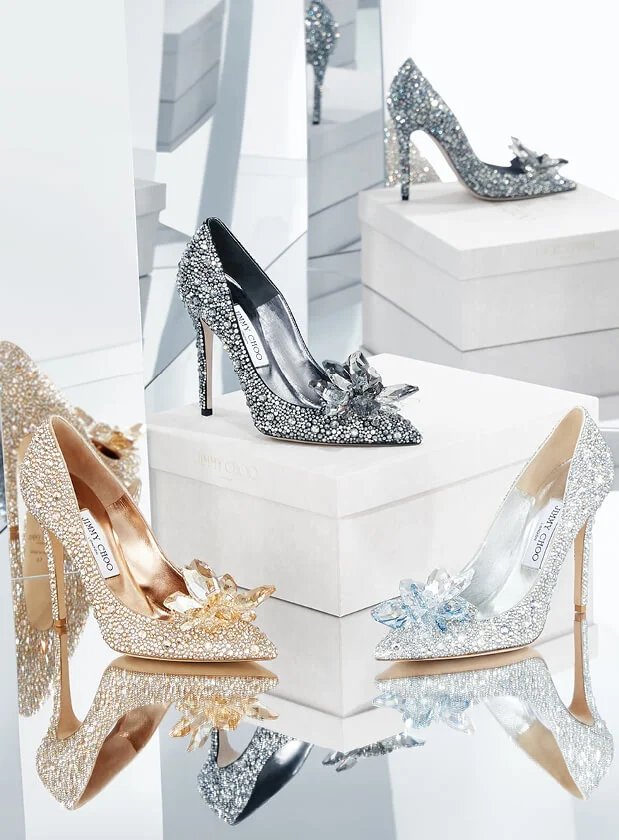 3 crystal embellished Jimmy Choo high heels, 1 black, 1 gold and 1 silver on mirrored background.