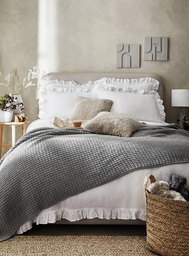 Double bed set up with white bedding, grey throw and fluffy beige cushions from The White Company.