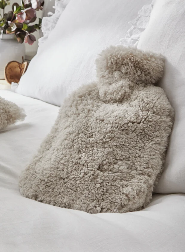 Fluffy beige hot water bottle on white bedding from The White Company.