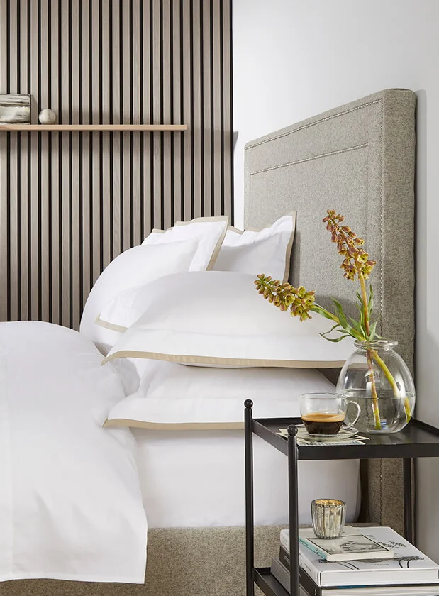Side shot of a double bed with beige headboard and white bedding from The White Company.