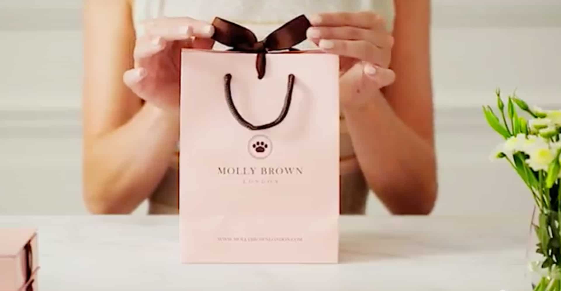 Molly Brown London bag on table being presented by slender feminine arms.