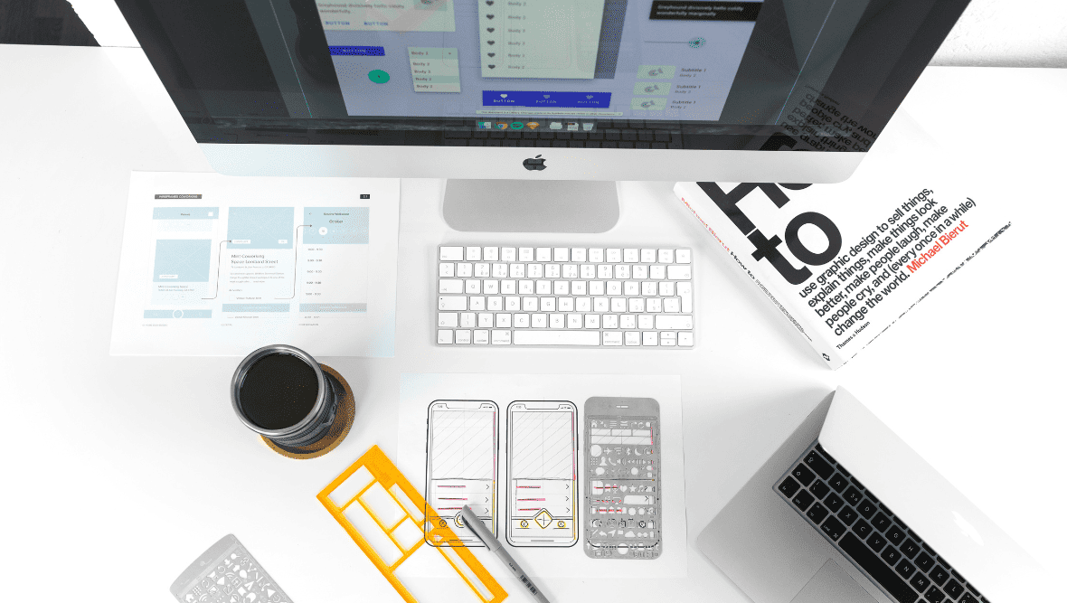 Birdseye view of a desk with a computer, keyboard, laptop and coffee.