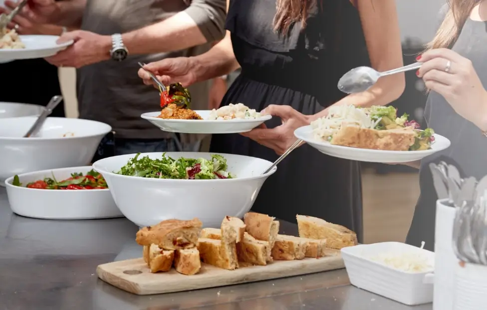 People holding plates to spoon buffet food on to.