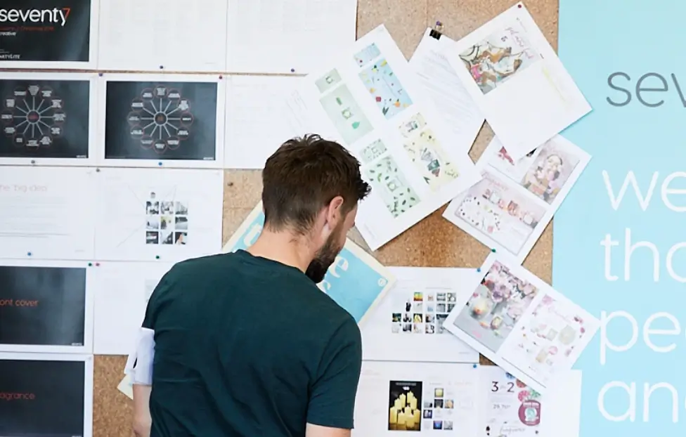 Seventy7 staff member looking at work pinned to pinboard.