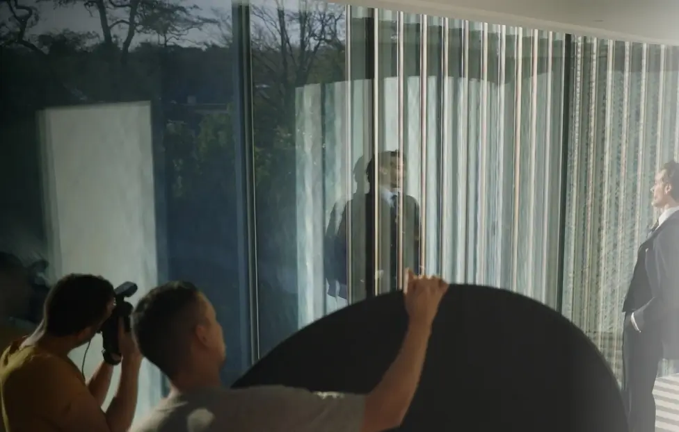 A photographer taking shots of male in suit with 3rd person holding a light reflector.