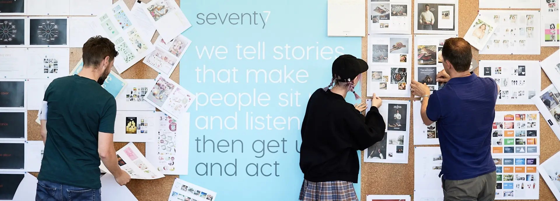 Members of Seventy7 staff adding work to oversized pinboard.