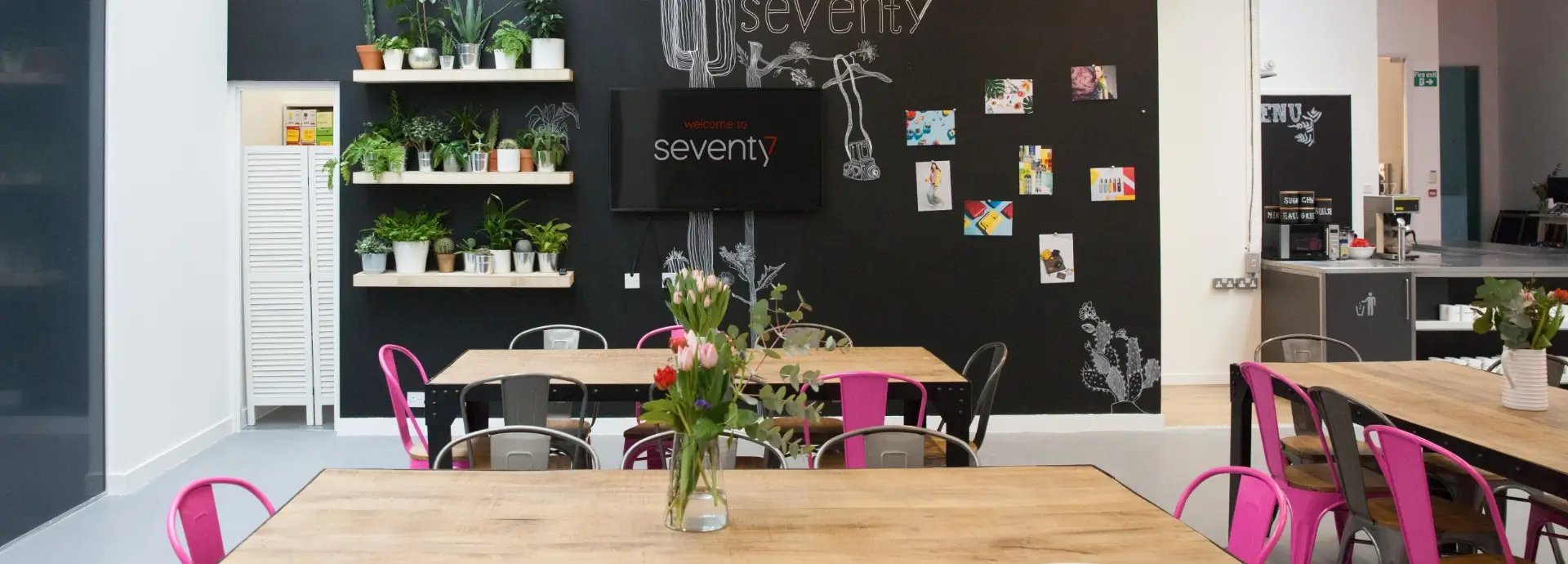 Wide shot of Seventy7 London communal area with tables, chairs and plant wall.