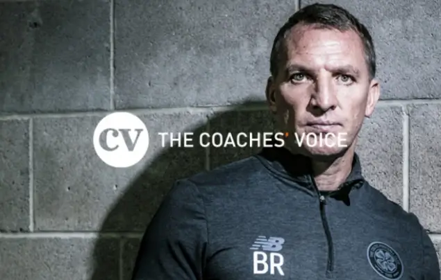 man looking directly at camera stood in front of grey wall with The Coaches' Voice logo in front of it.