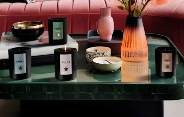 PartyLite CBD candles on green table with pink sofa in the background.