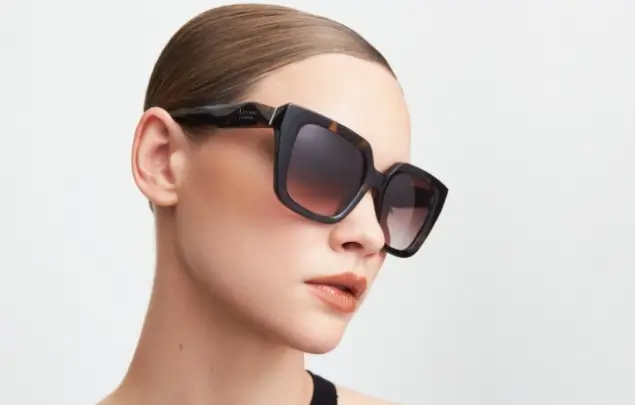 Female model wearing oversized shades in front of white background.