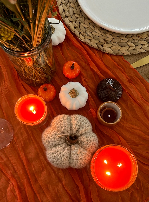 An overhead shot of 2 lit PartyLite candles with some decorative knitted and ceramic pumpkins.