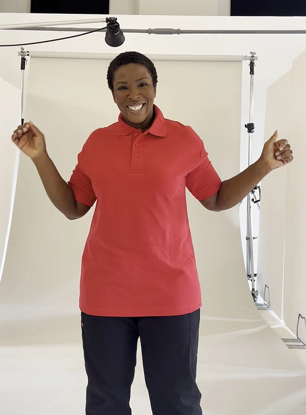 Woman in a neutral photography set wearing a red Simon Jersey polo top and black trousers.